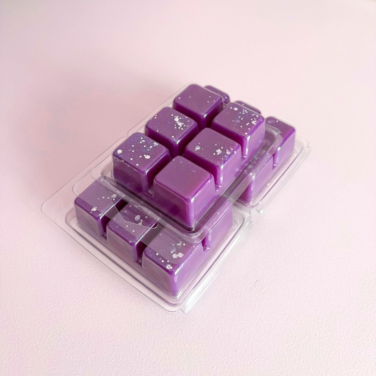 Purple wax melts in a clear plastic mold on a light pink background